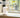 A small, white indoor camera device sits on a light wood shelf next to a small potted succulent plant