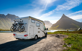 White RV parked by scenic mountains and tranquil lakeside, ideal for road trips, outdoor travel, and adventure vacations.